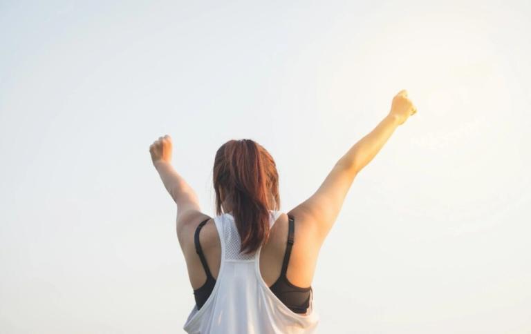 a lady lifting her hands to the sky on a bright sunny day as part of wellness