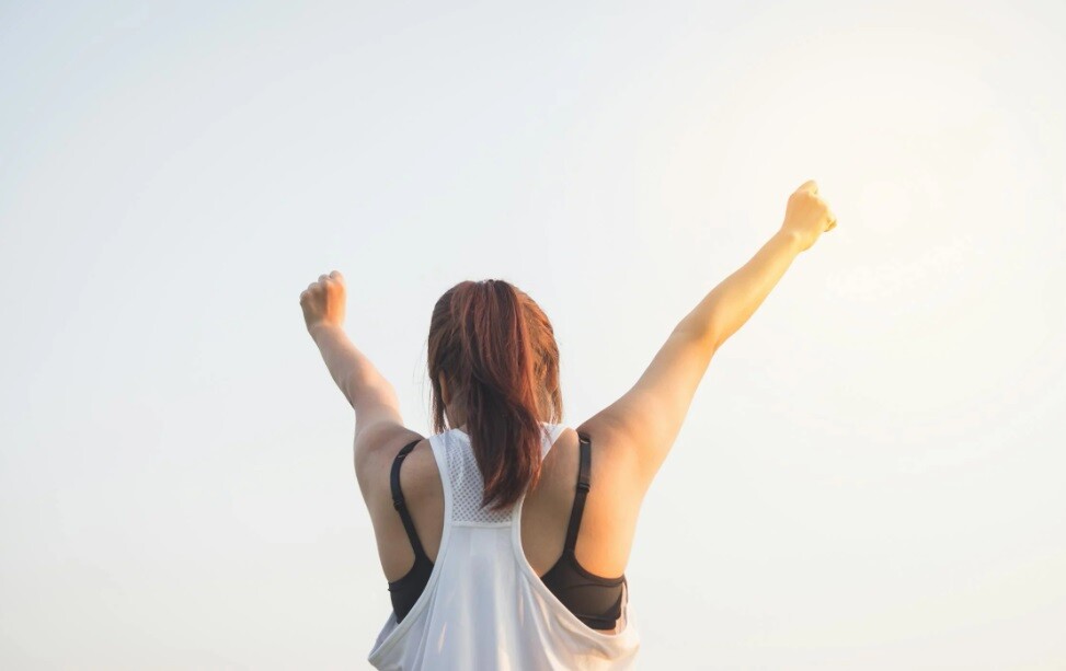a lady lifting her hands to the sky on a bright sunny day as part of wellness