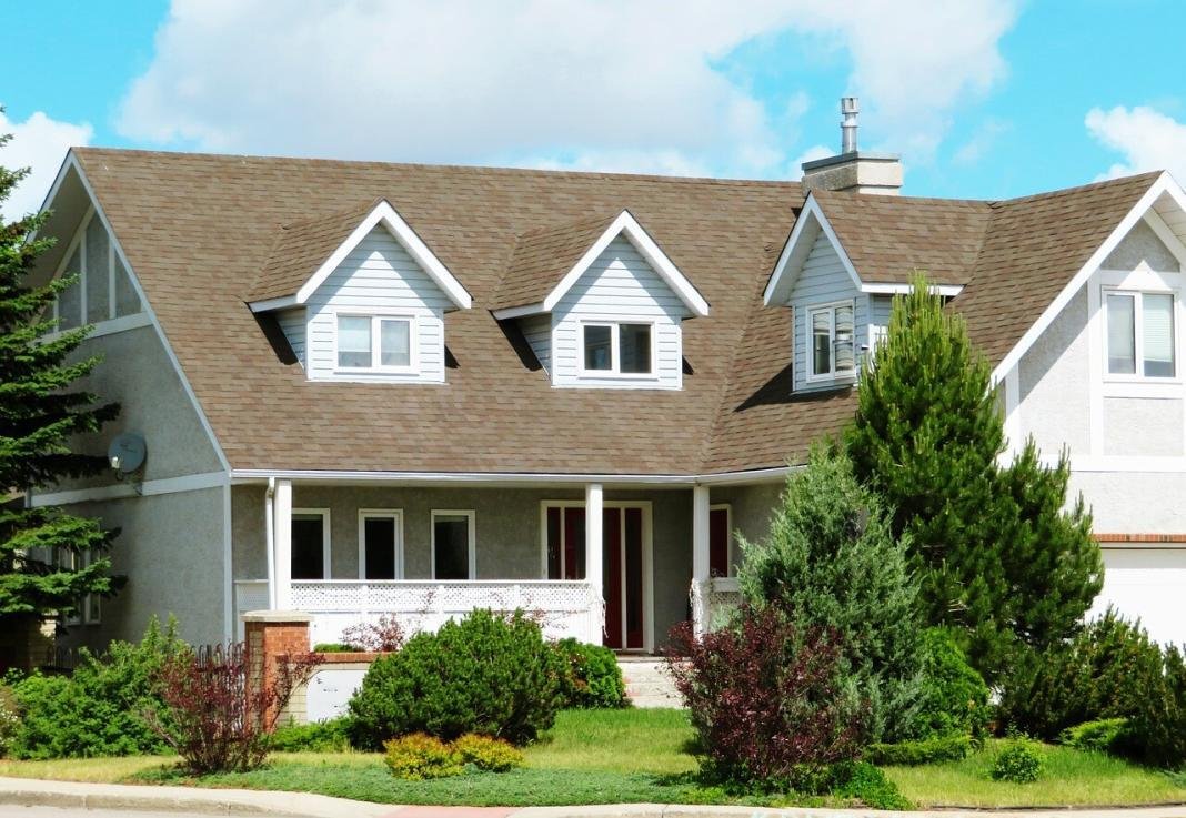 A two storeyed beautiful house with two tress and an awesome garden. Clear blue is in the background.