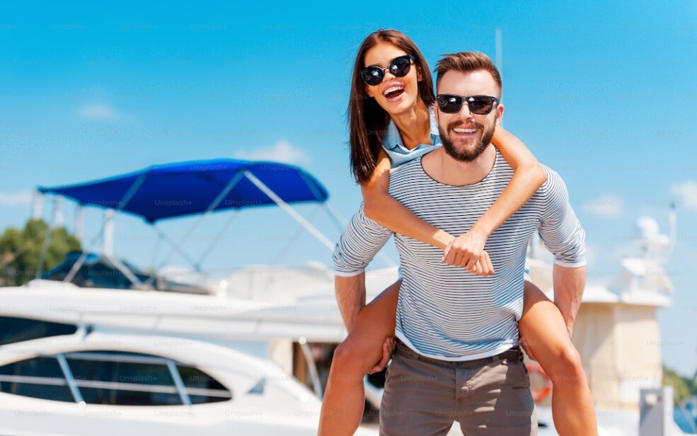 a man carrying a woman on his hip and behind them is a yacht signifying zero waste holidays
