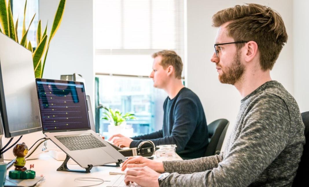 two persons looking at the desktop screens and sitting on the chairs signifying zero waste office