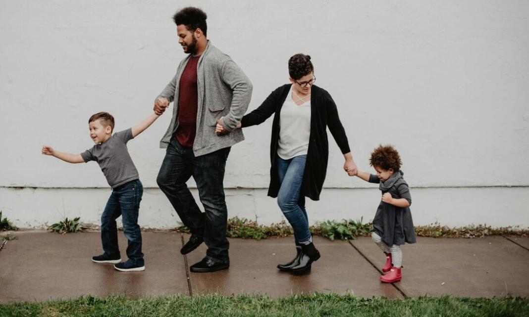 a father, a mother and two kids walking beside a house with white background wall signifying zero waste parenting