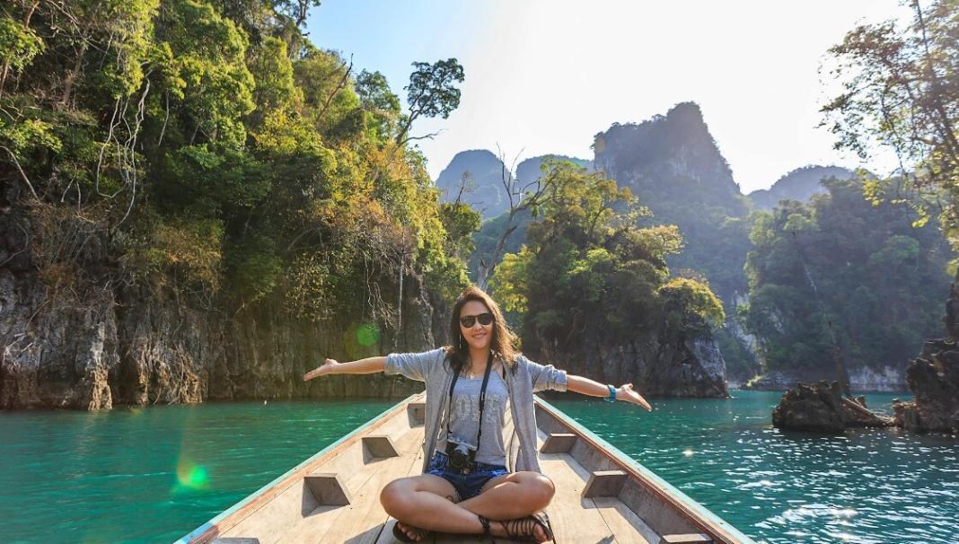 a lady stretching her hands with joy on a boat with mountain and trees behind her signifying zero waste travel