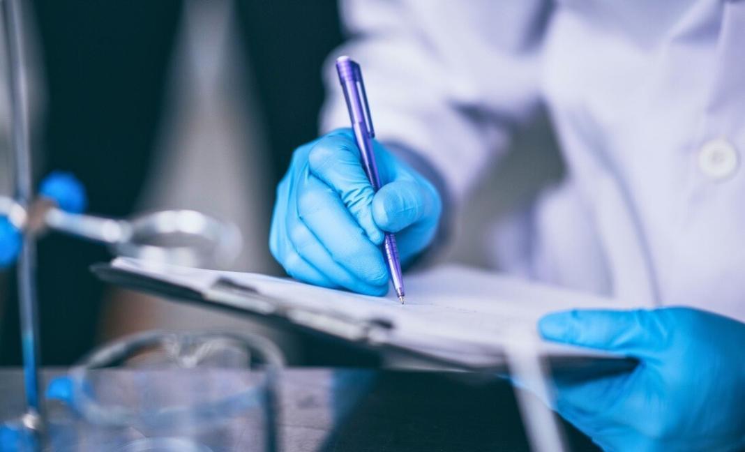 a person recording the lab results with a pen on a sheet of paper in healthcare industry