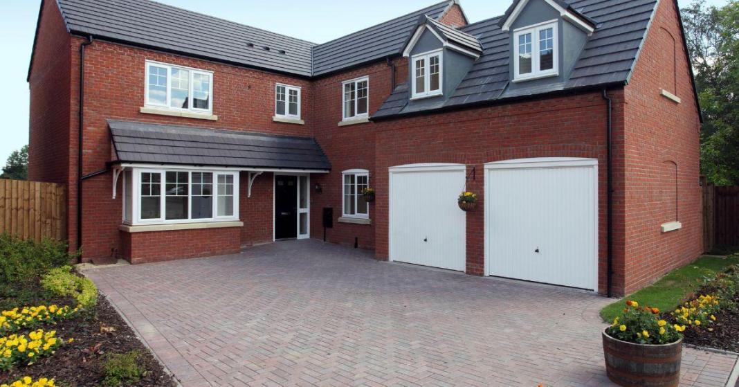 a two storeyed house with brown bricks and white car sheds