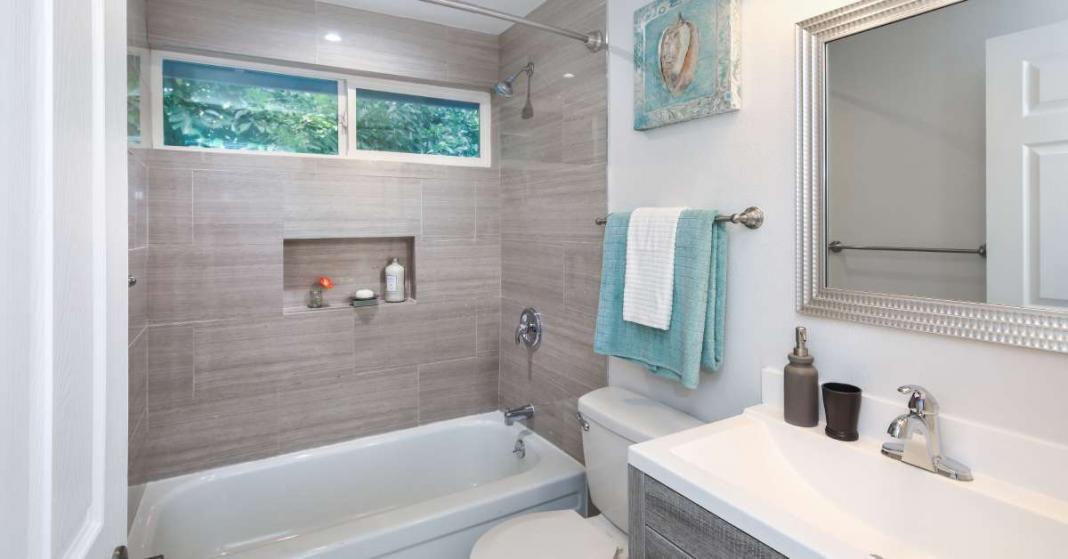 An upgraded bathroom contains a white bathtub, a white toilet, and a modern vanity. The white walls contain beach artwork.