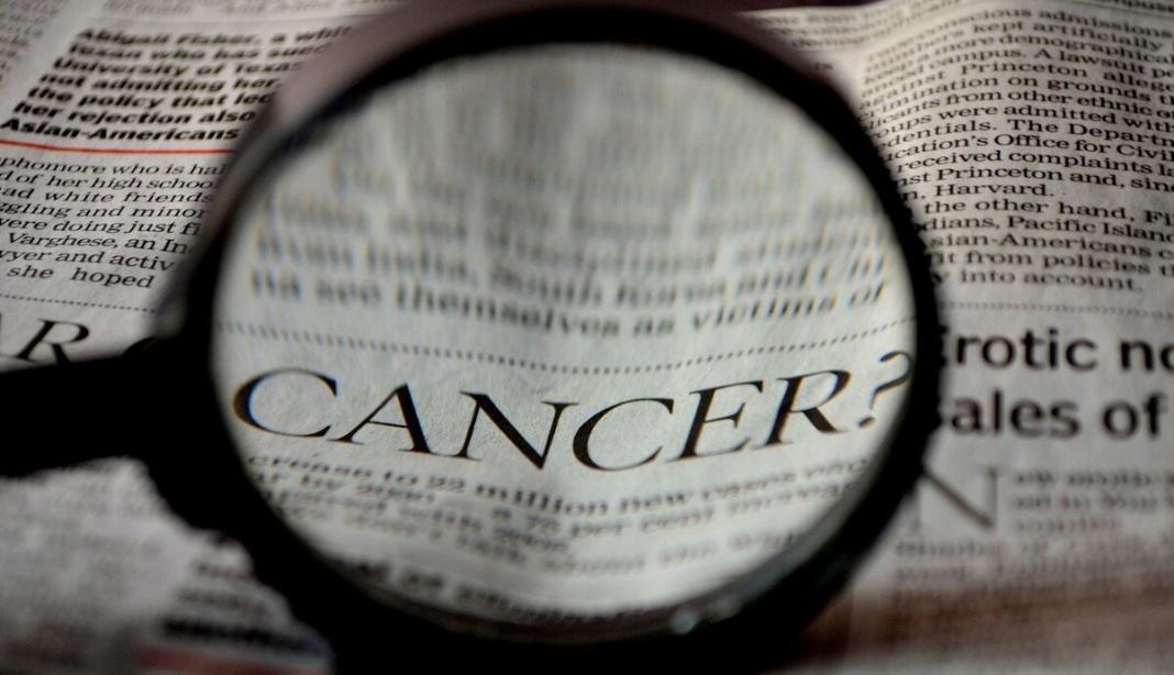 a magnifying lens projected on a newspaper highlighting the word cancer