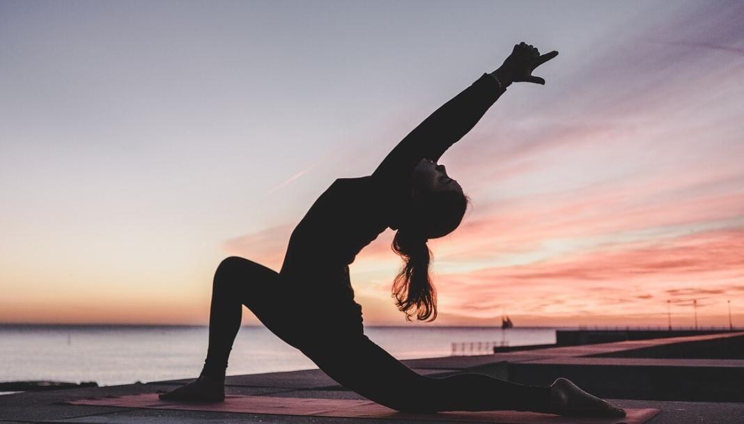 a lady posing a yoga step in a sunset background 