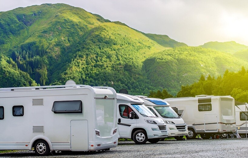 four caravans are standing on the road with green mountains and sky in the background