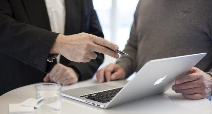 a person pointing to a laptop and explaining points to another person