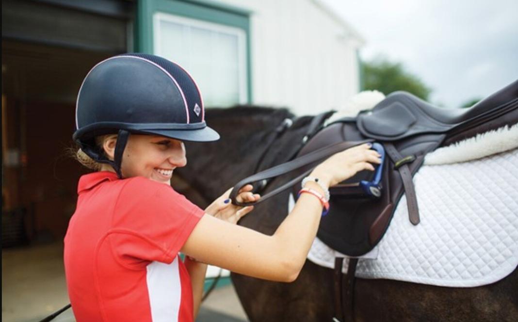 a lady wearing a helmet climbing on the horse for riding