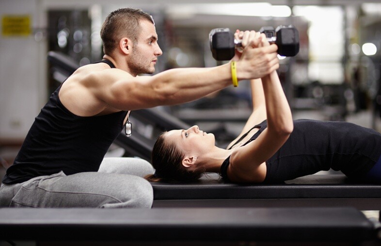 a man training a lady who is exercising with dumb bells