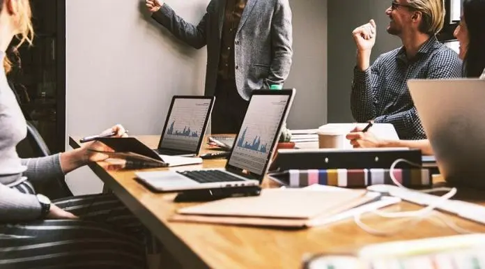 person explaining concepts on a white board with laptops and books on the office table