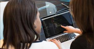 a lady pointing to the laptop and explaining the software to another lady looking at it