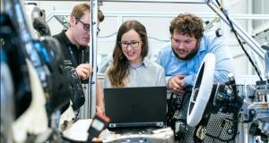 three people looking at a laptop that is placed in a manufacturing assembly unit