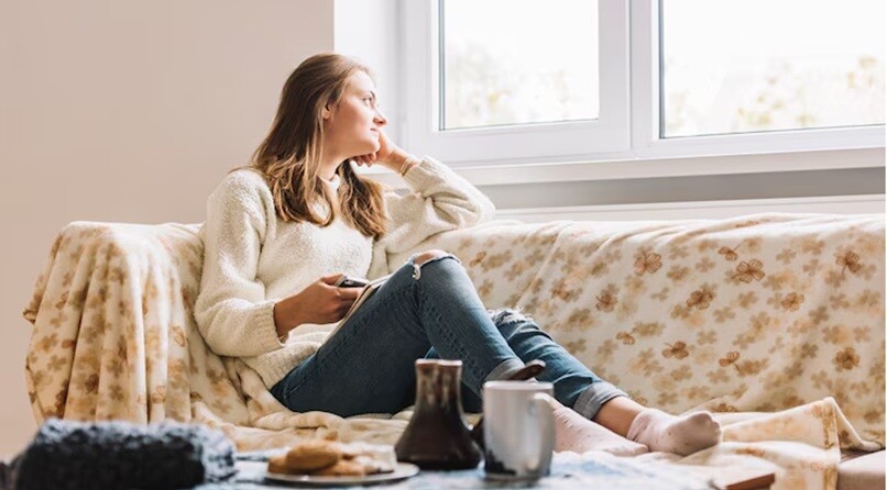 a lady sitting on a sofa and looking outside the window of the house