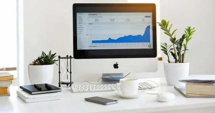 a monitor screen with graphs placed on a table with tea cup, notepad and keyboard