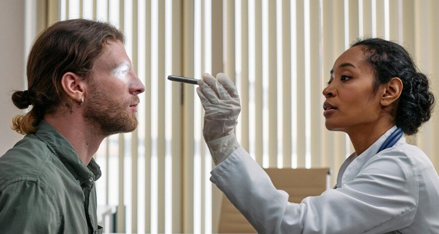 an eye doctor checks a patient in the eyes using a light torch
