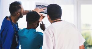 a doctor pointing to a medical photo with two other persons looking into it