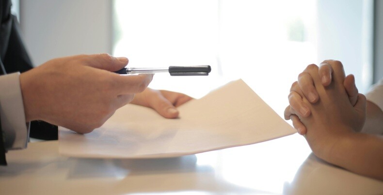 a person's hand pointing with a pen as if a formal discussion is in progress with another person