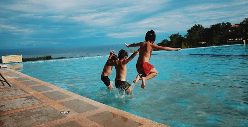 three kids jumping into a swimming pool in an evening sunset