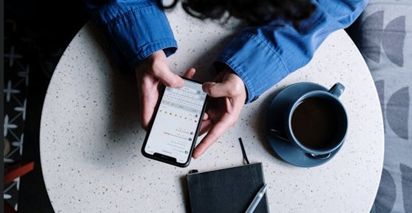 a person holding a mobile and texting placing hands on a table with tea cup and a diary beside
