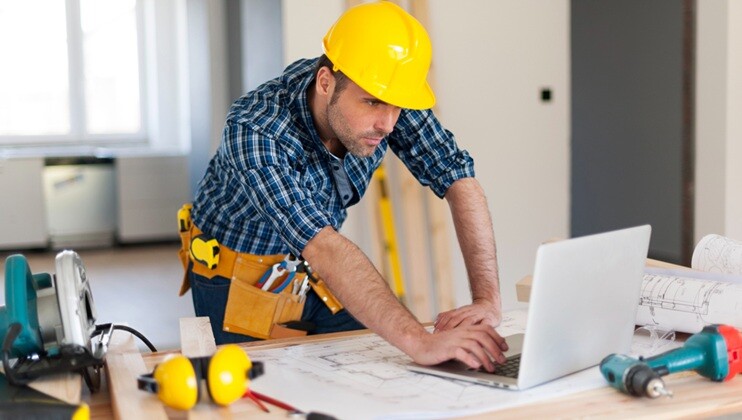 a construction engineer using a laptop and wearing a yellow helmet