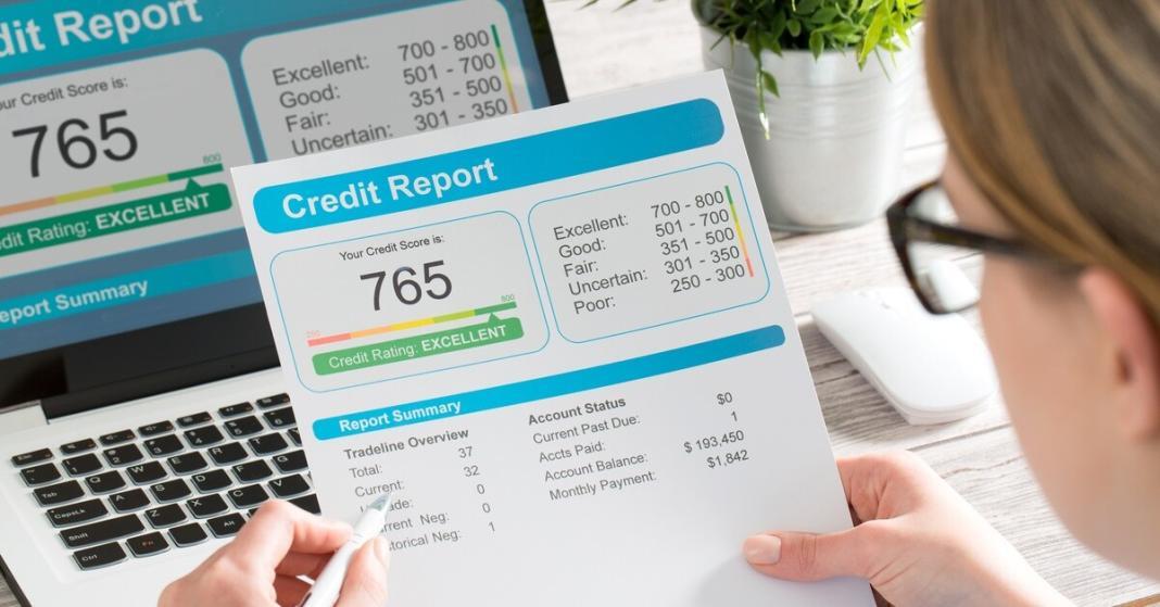 A person sitting at the table with their credit report printed on a paper. Their pencil is pointing to a 765 credit score.
