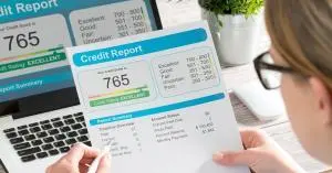 A person sitting at the table with their credit report printed on a paper. Their pencil is pointing to a 765 credit score.