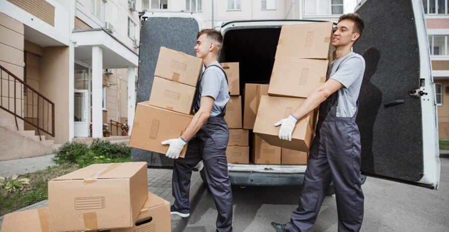 two persons carrying cartons from a van to a house