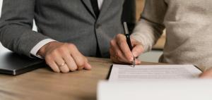 legal documents being signed by a person and another person standing beside