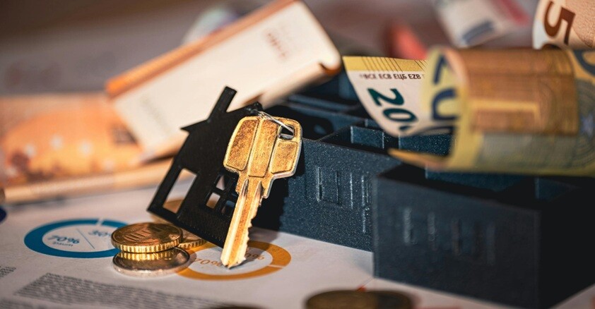a key and a house placed on a table with papers and money