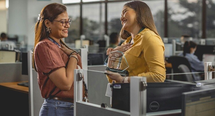 one lady congratulating another lady for her best performance award in an office