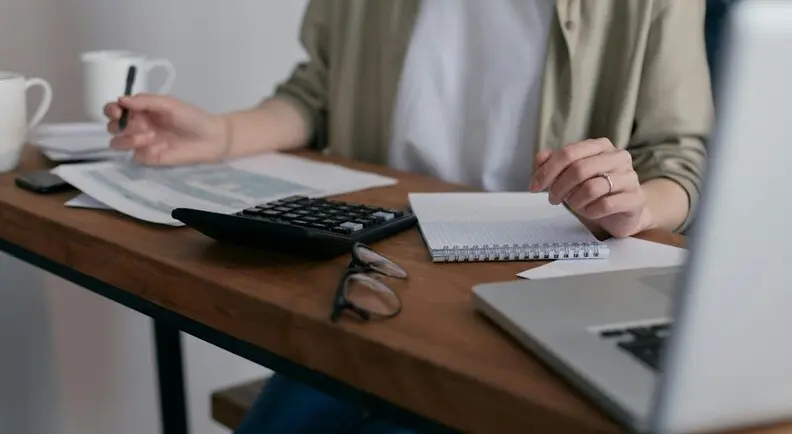 a lady doing accounting with calculator, laptop, pen and notepad