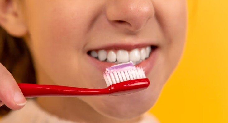 a girl brushing her teeth with brush and paste