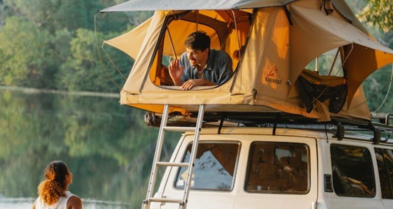 a camp set up on top a jeep with a person inside it and a lady looking at him
