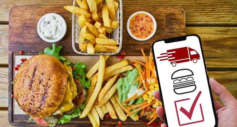 burger, frensh fries and sauce place don a table with a mobile phone showing the food delivery status