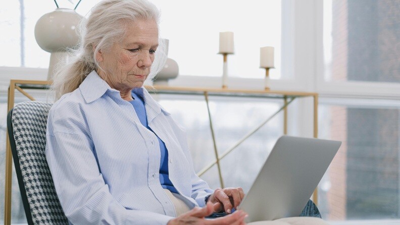 elderly woman an elderly woman having white hair using a laptop sitting on a chair with white shirt