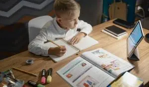 a kid studying using books on a table with pens and mobiles placed beside