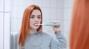a lady brushing her teeth by looking at a mirror