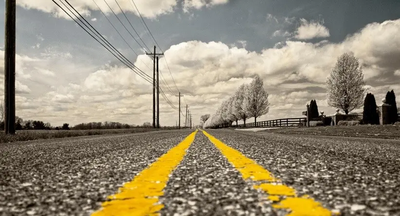 yellow lines drawn on a highway road and clear sky and plants seen in the background