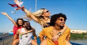 A group of four friends, the women are on the backs of the men for piggy back rides. They're all smiling and happy.