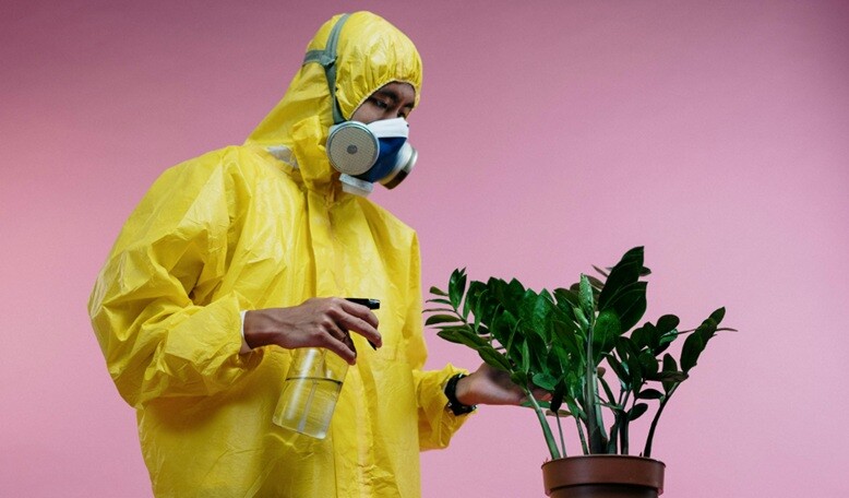 a person wearing an air purifier mask is watering a plant with pink background