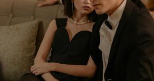 a lady in black dress wearing a diamond necklace and an handsome man sitting beside