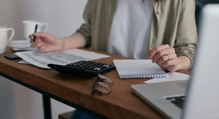 a lady computing the tax information using a notepad and a laptop