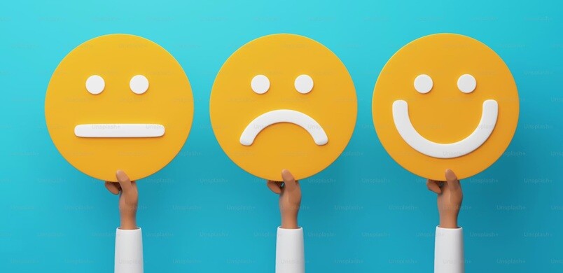 three hands each holding a face, one is neutral, one is sad, and one is happy