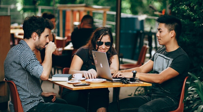 three people sitting on a table and discussing on the projects using laptops
