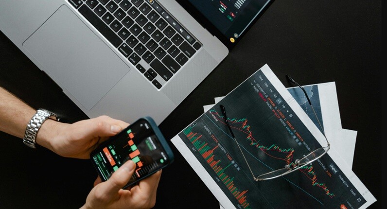 a person holding a mobile with stock market charts and laptop