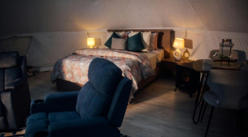 a recliner seen in blue color with bed and pillows present in the bedroom