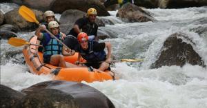 four people sitting inside a raft which is sailing on the waterfalls in between the rocks